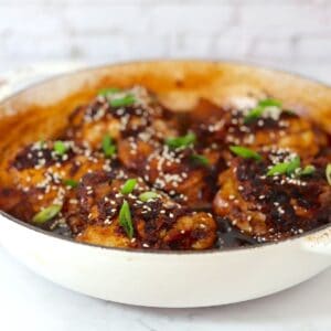 Ginger braised chicken thighs in a skillet topped with sesame seeds and green onions.