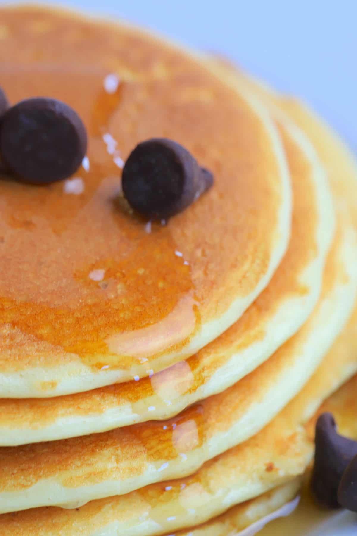 stack of protein powder pancakes on a white plate, topped with sugar free maple syrup and chocolate chips.