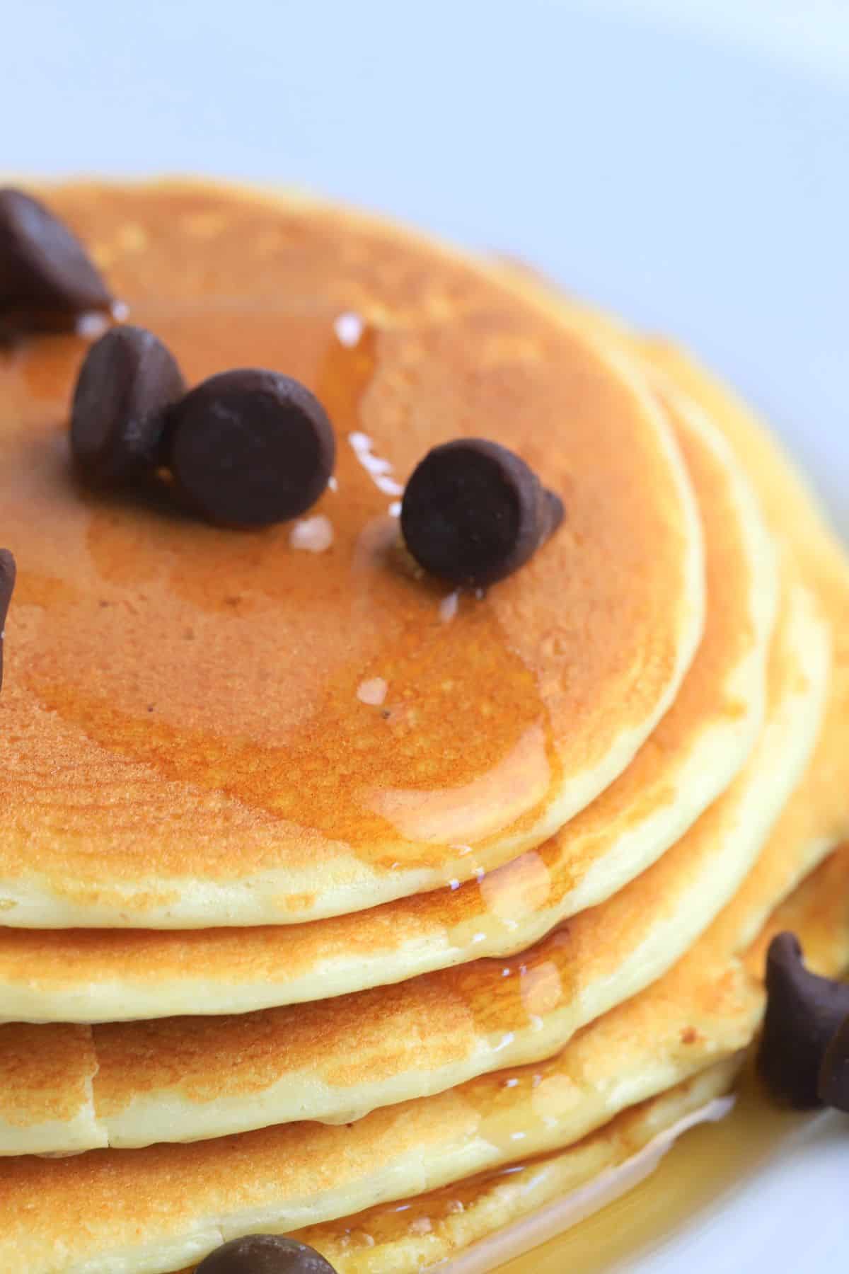 stack of protein powder pancakes on a white plate, topped with sugar free maple syrup and chocolate chips.