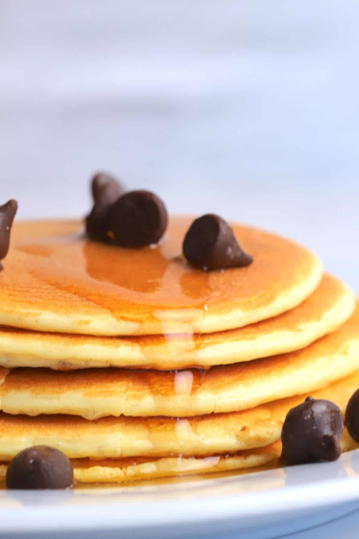 stack of protein powder pancakes on a white plate, topped with sugar free maple syrup and chocolate chips.