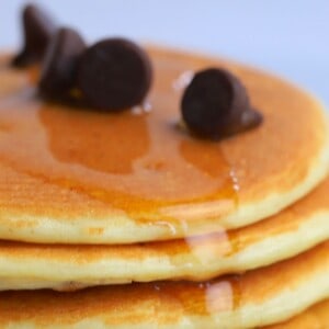 stack of protein powder pancakes on a white plate, topped with sugar free maple syrup and chocolate chips.