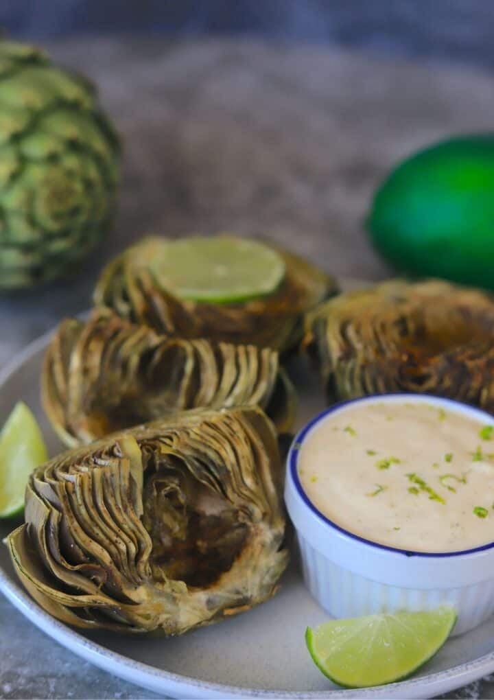 artichokes on a plate with dipping sauce and limes