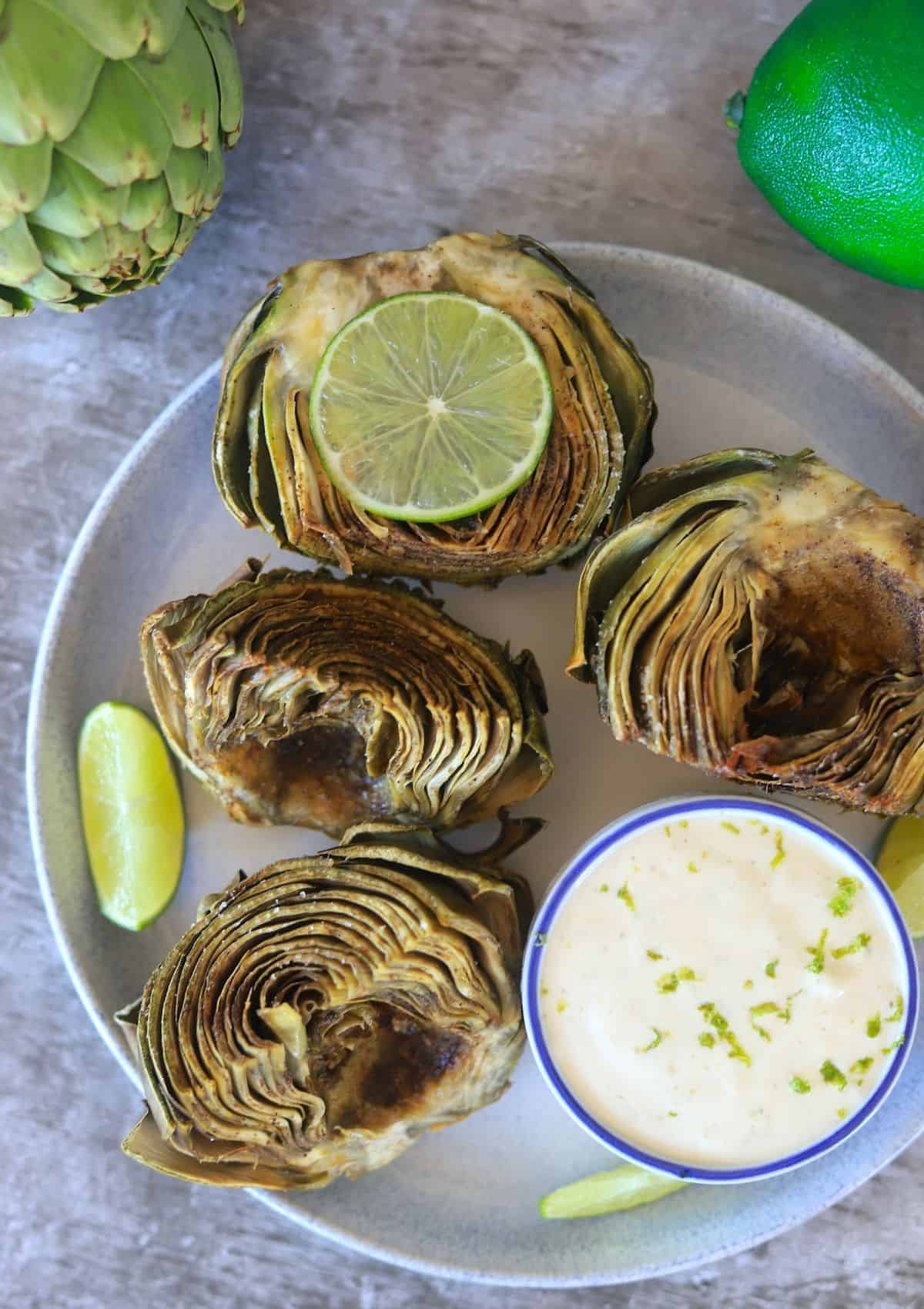 artichokes with dipping sauce and lime wedges