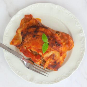 Lasagna on a plate with a fork and basil leaves on top