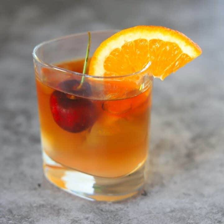 old fashioned cocktail with a cherry and orange wedge in a tumbler