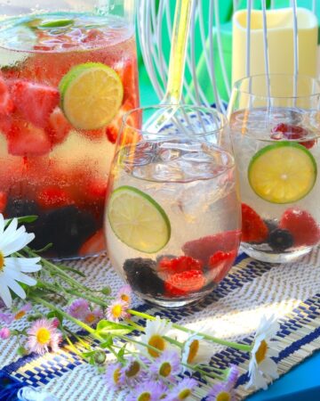 a pitcher of sangria with two glasses outdoors with flowers