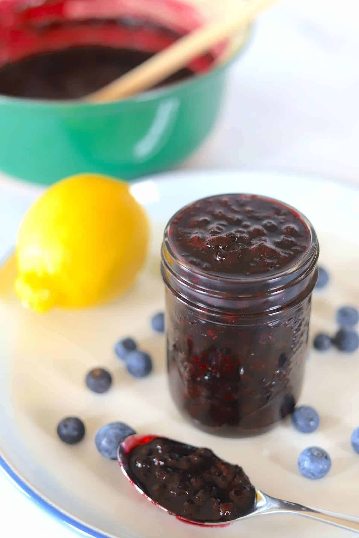 blueberry sauce in a mason jar on a plate with fresh blueberries and lemon