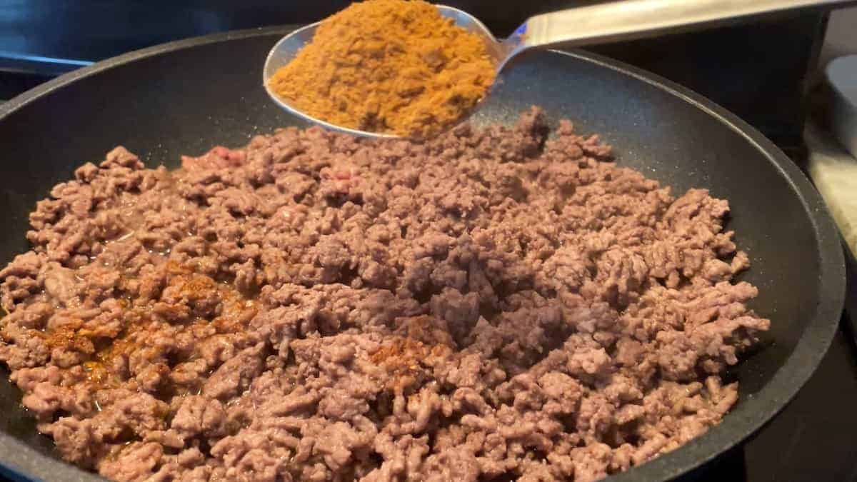 browning taco meat on stove and adding spoon of chili powder