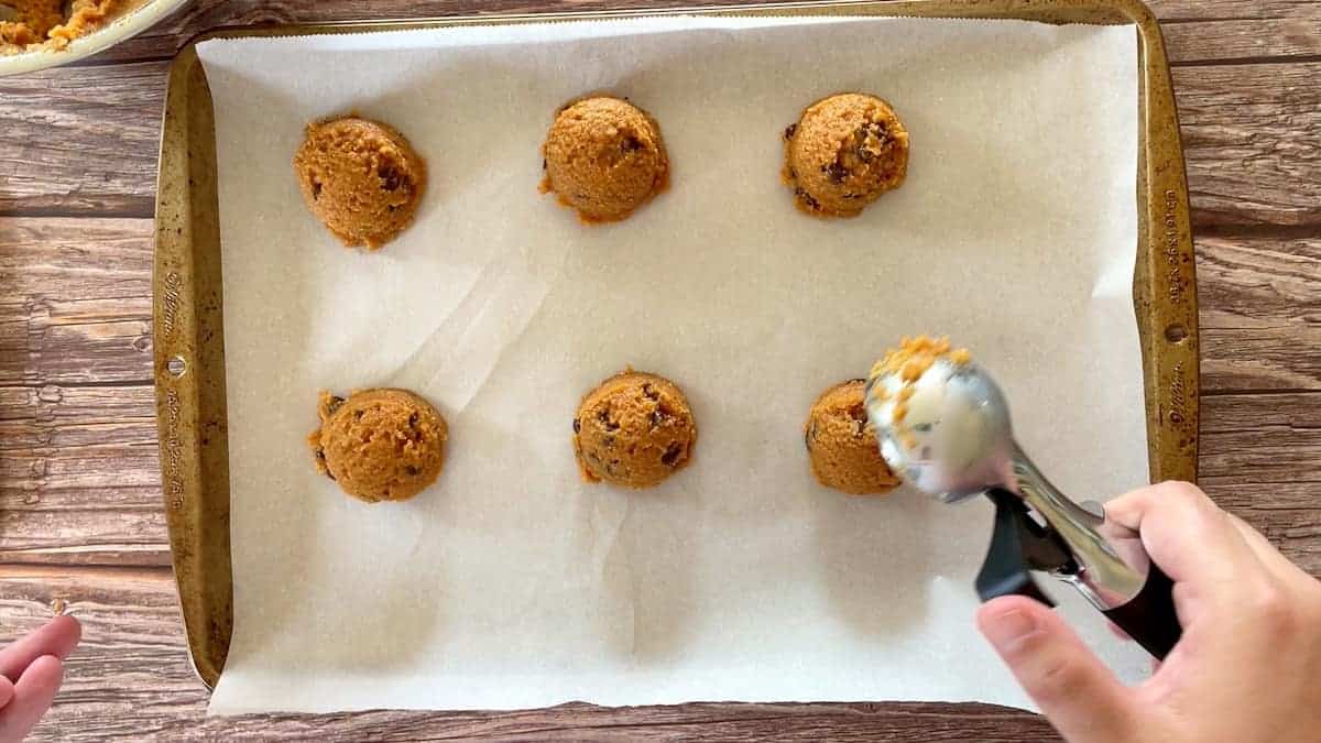 placing cookie dough onto a parchment lined baking sheet with an ice cream scoop