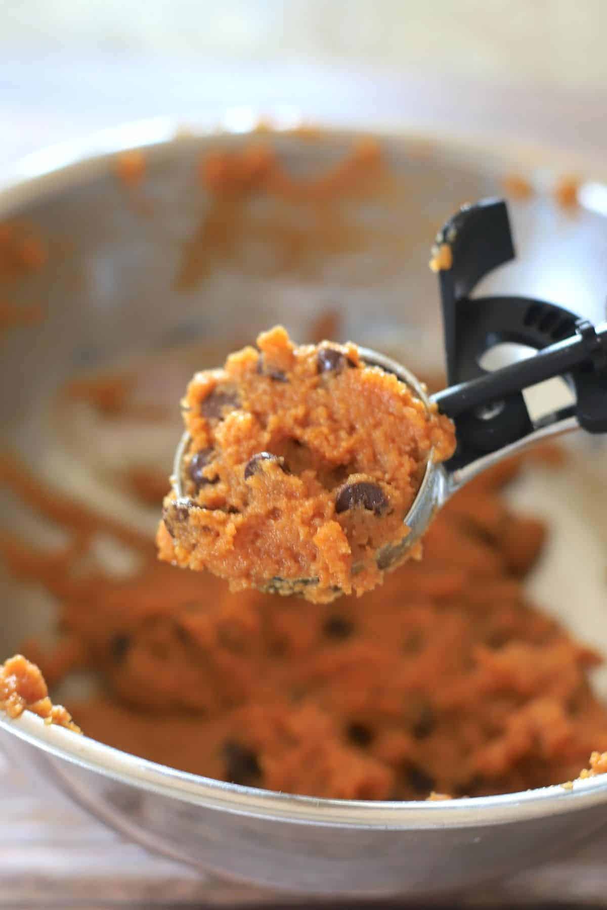 cookie scoop with dough above a bowl with cookie dough