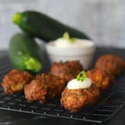 zucchini fritters on a cooling rack topped with sour cream and onion with a dipping bowl and 2 raz zucchinis