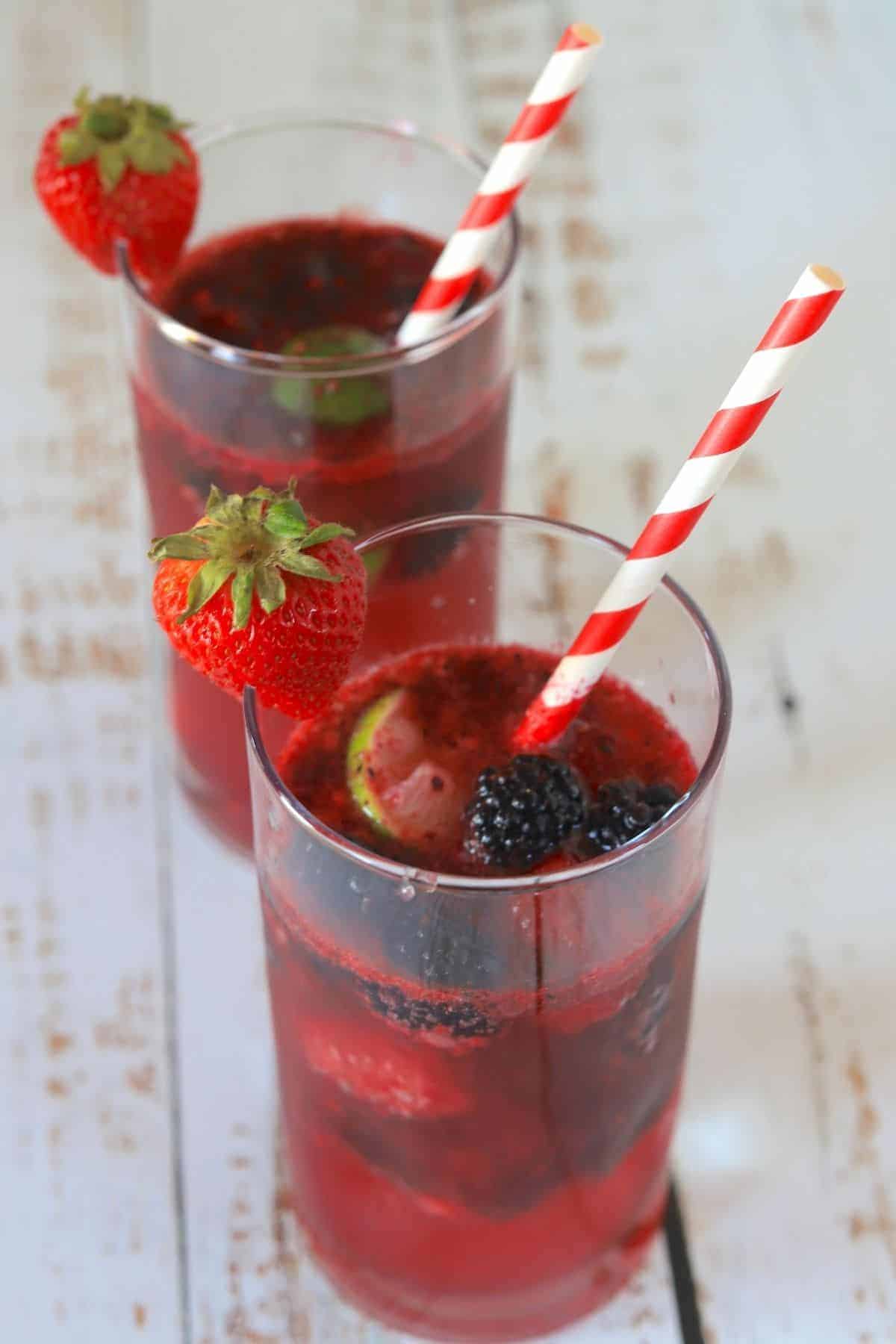 2 tall glasses filled with berry daiquiris a straw and garnished with a strawberry