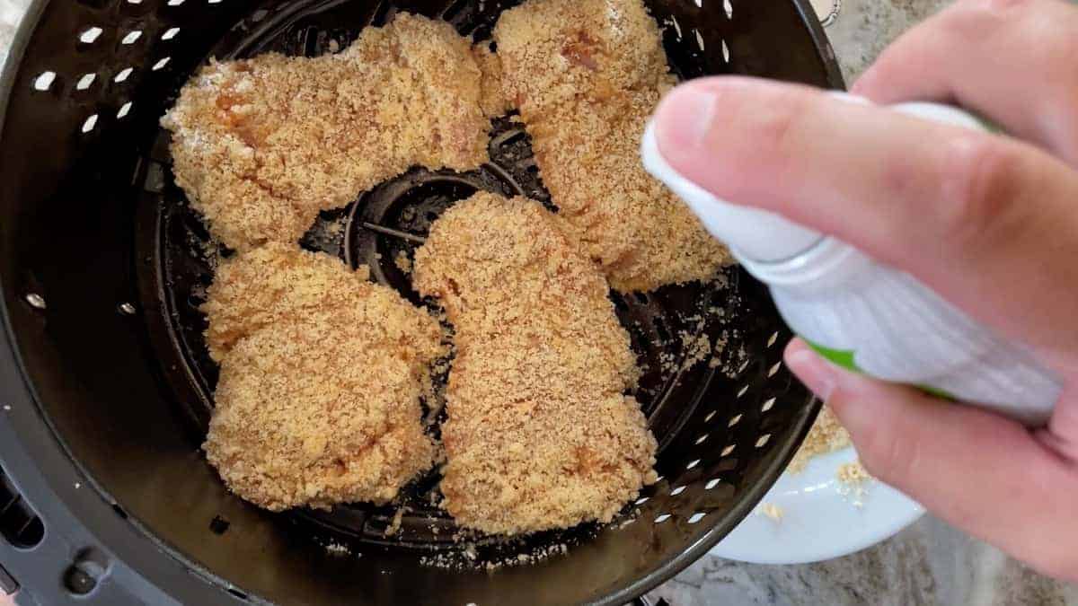 Chicken in air fryer basket being sprayed with cooking spray