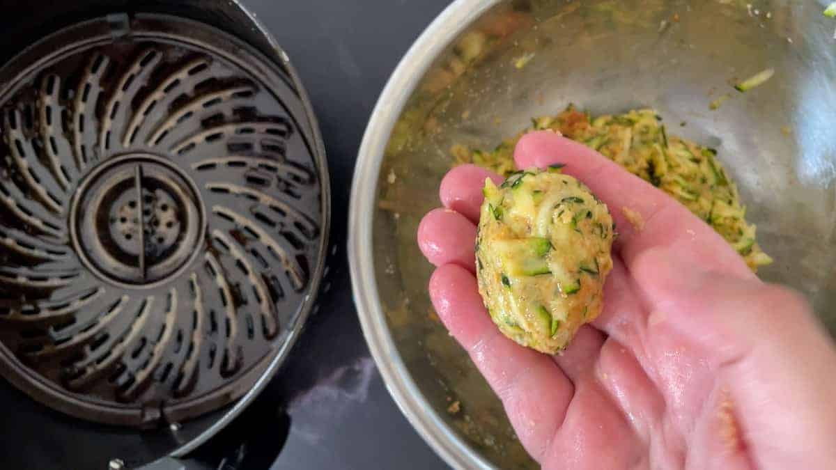 raw zucchini rolled into shape above a bowl next to air fryer basket