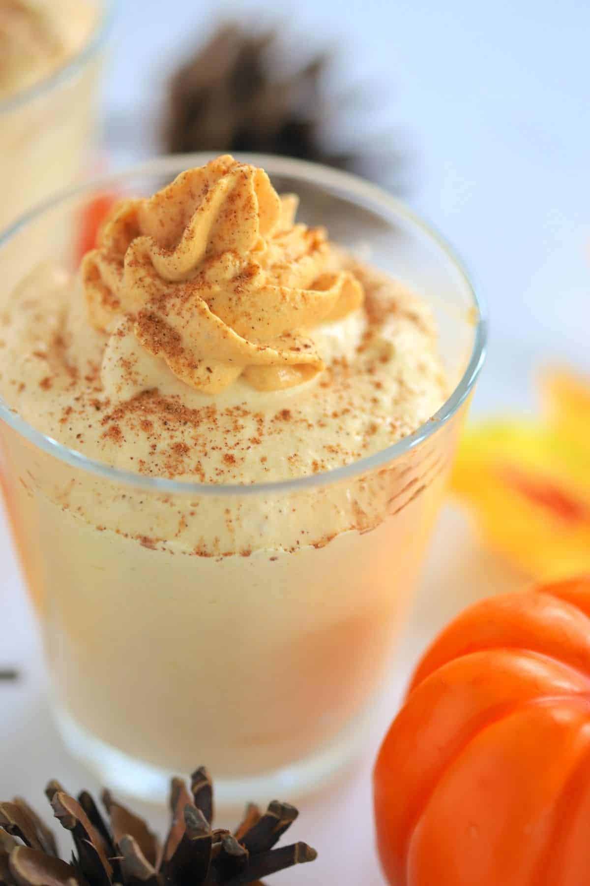 pumpkin mousse in a glass topped with whipped cream next to acorns and a pumpkin