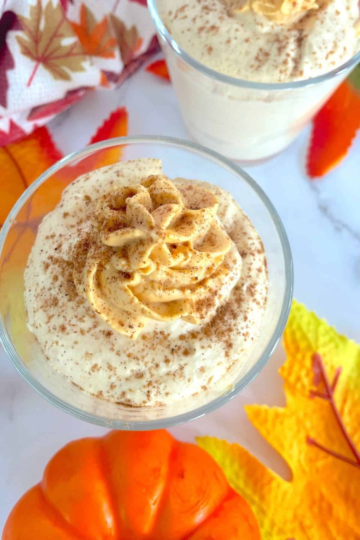 pumpkin mousse in a glass shot from above with fall leaves and a pumpkin