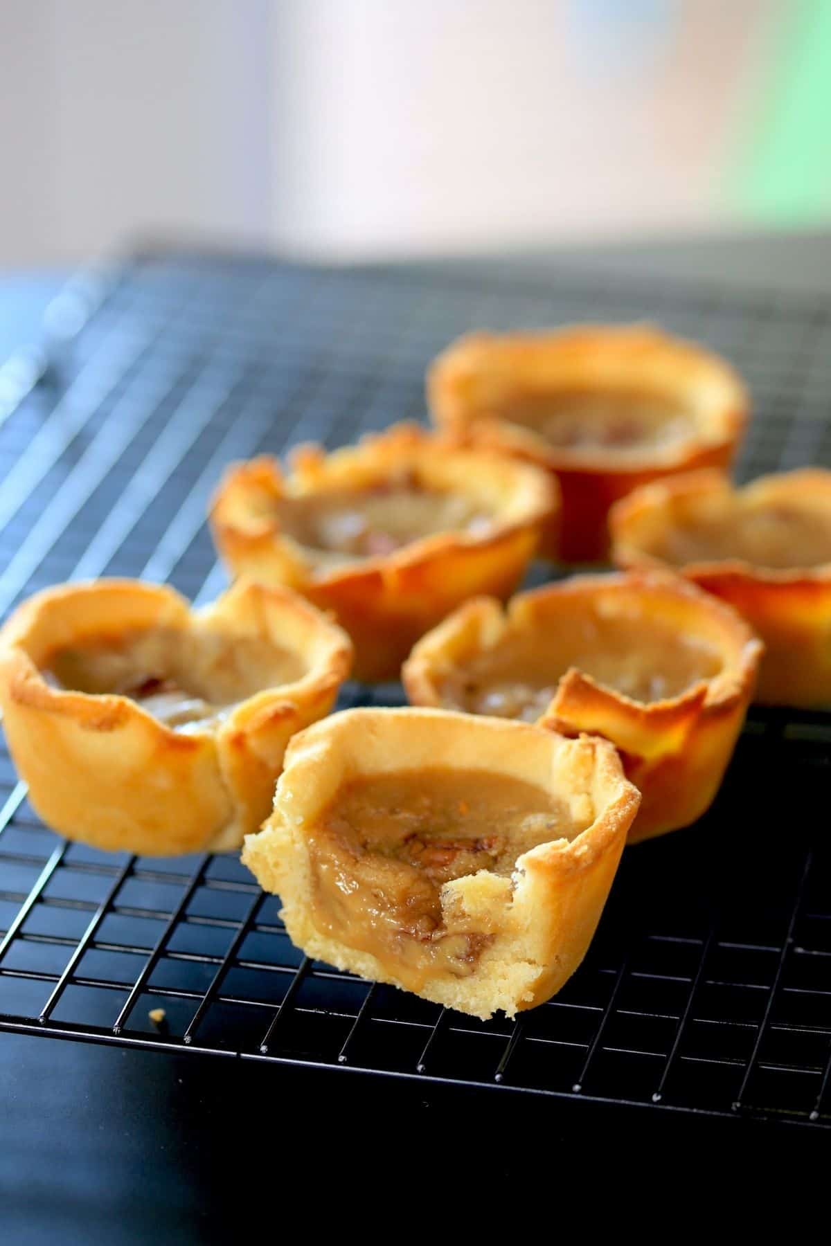 6 golden butter tarts with one sliced to show the gooey filling