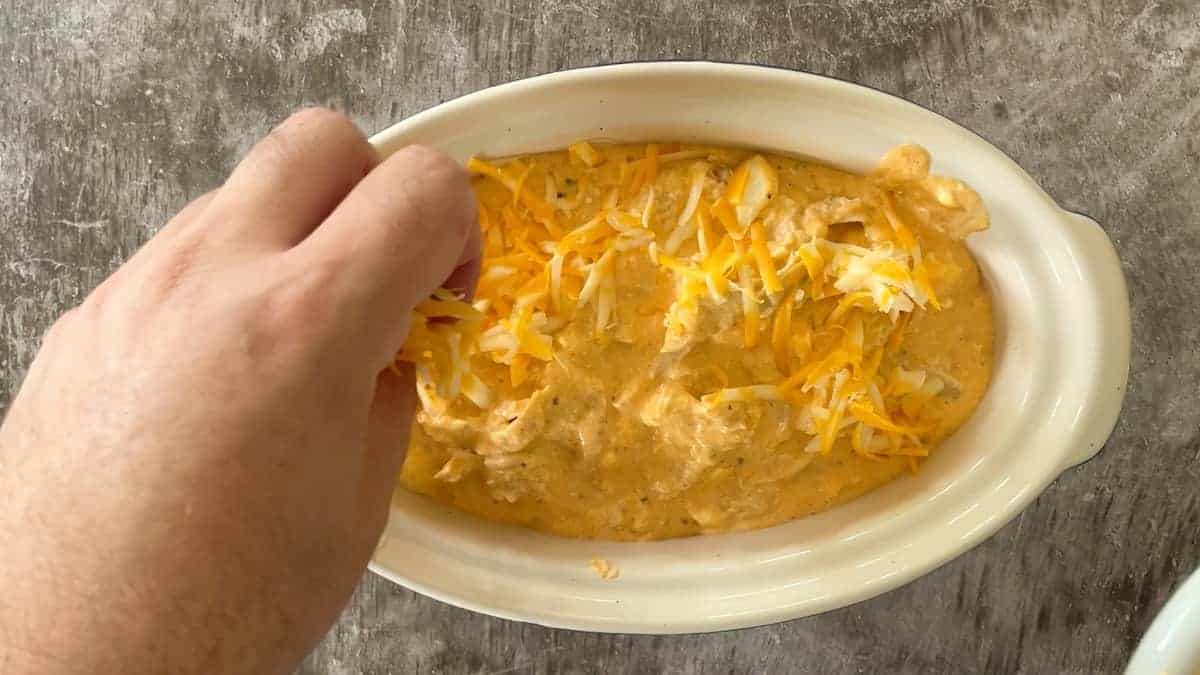 topping the dip with cheddar in a large casserole dish