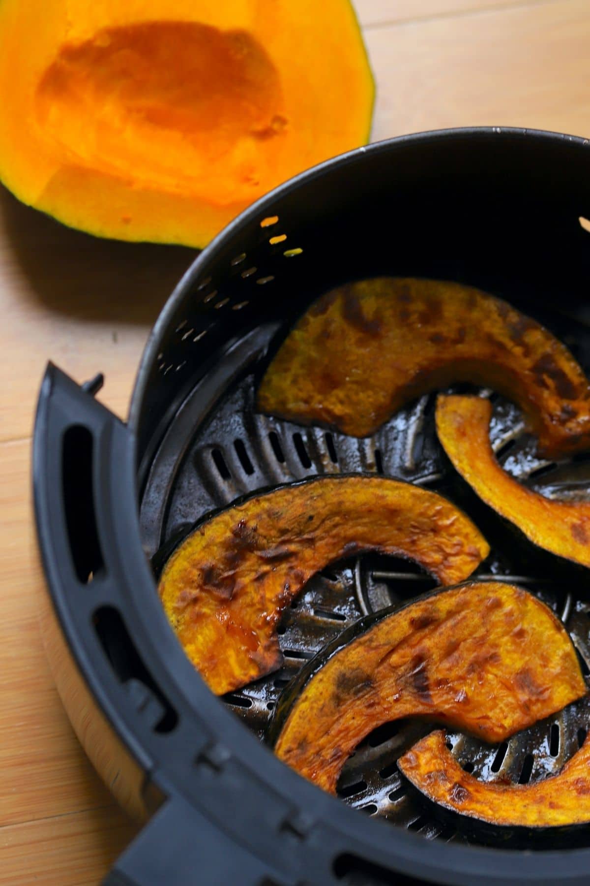 kabocha squash wedges cooked in the air fryer basket with a raw squash above