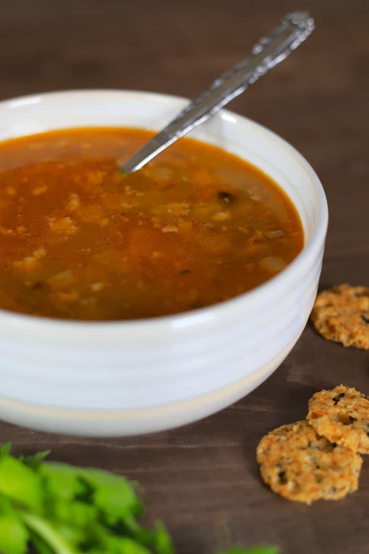 white bowl with chicken soup and a spoon with side of crackers and celery leaves