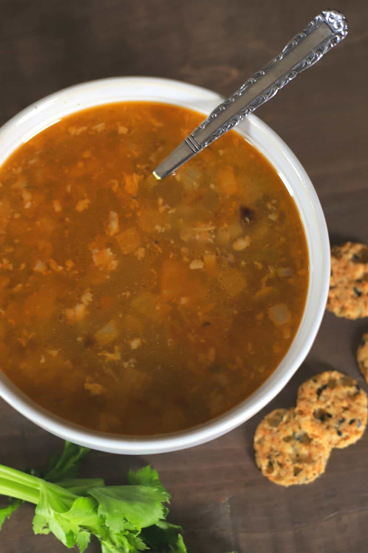 white bowl with chicken soup and a spoon with side of crackers and celery leaves