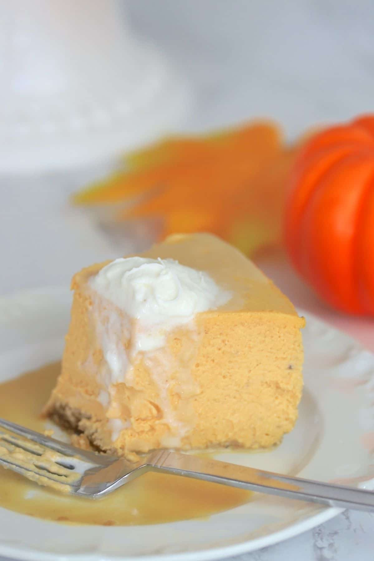 plate with half a cheesecake topped with whipped cream and a fork on the side and a pumpkin