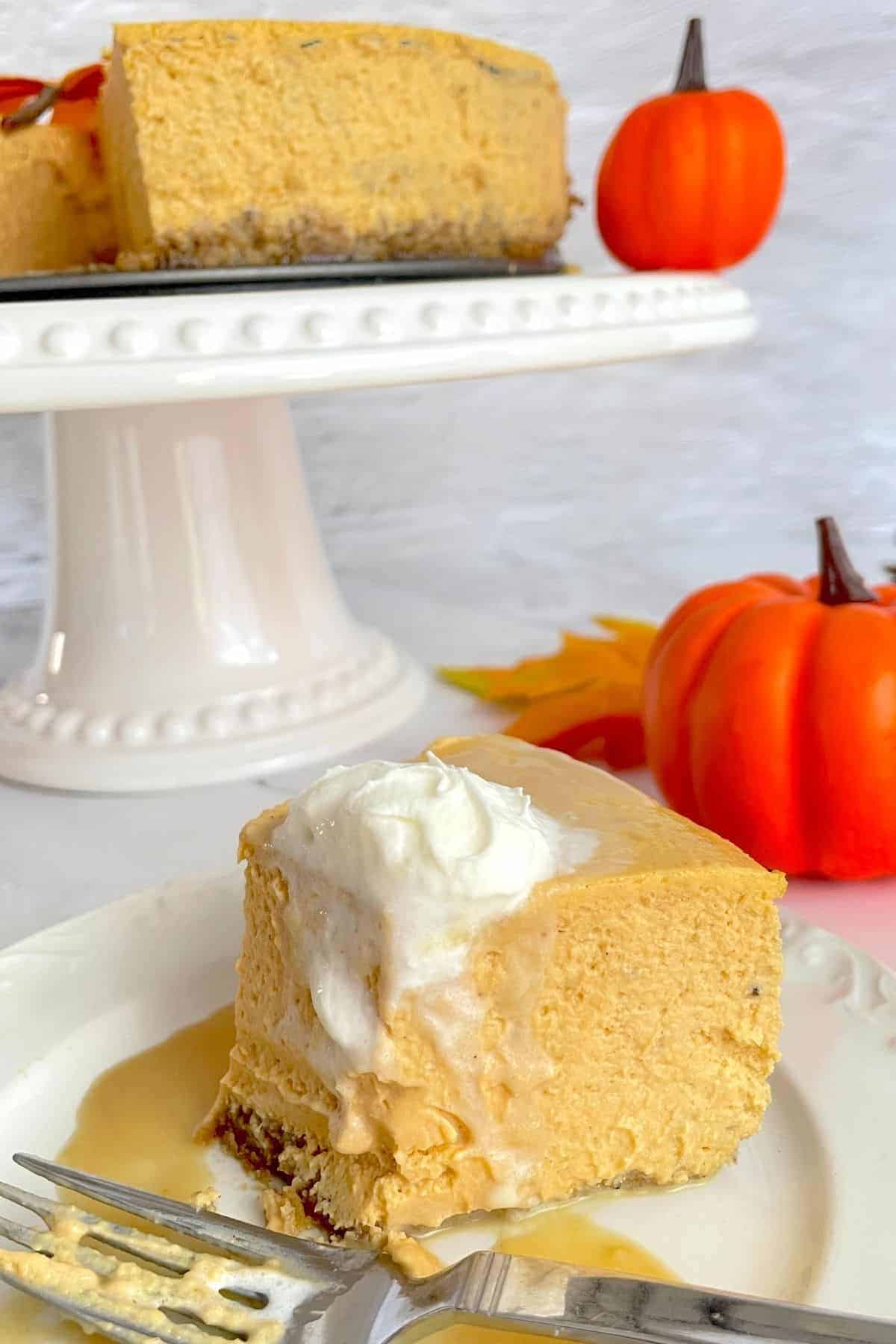 plate with half a cheesecake topped with whipped cream and a fork on the side with full cheesecake and a pumpkin