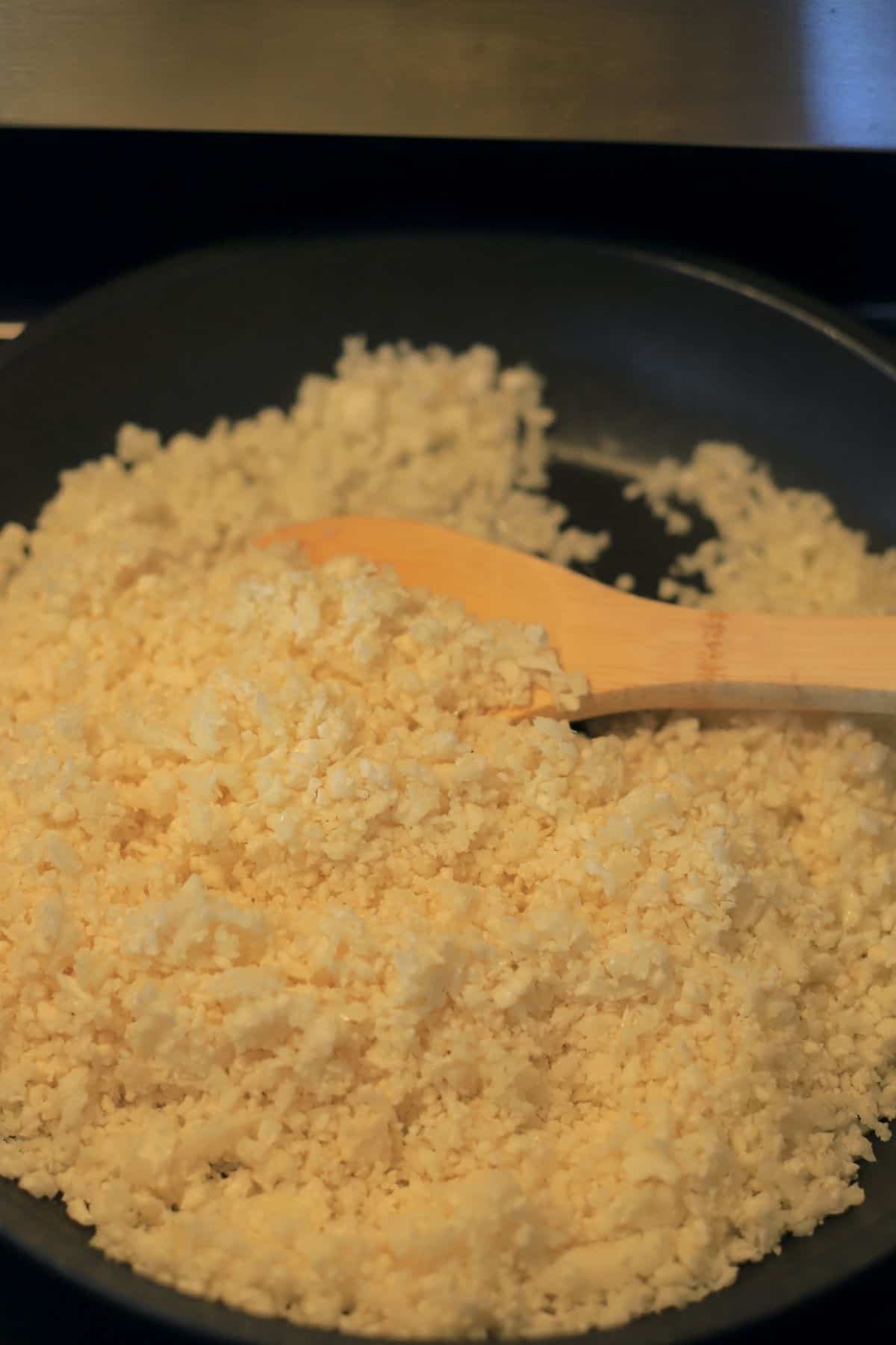 cauliflower rice in a pan with a wooden spoon