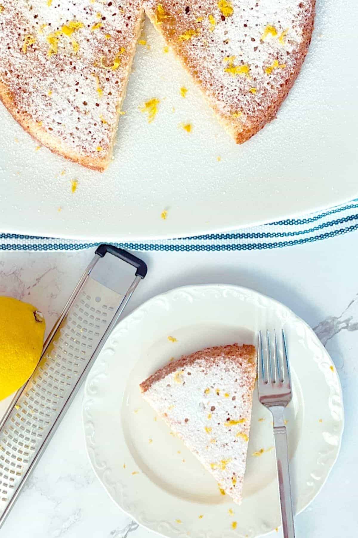 Lemon cake on a plate next to a lemon and lemon zester 