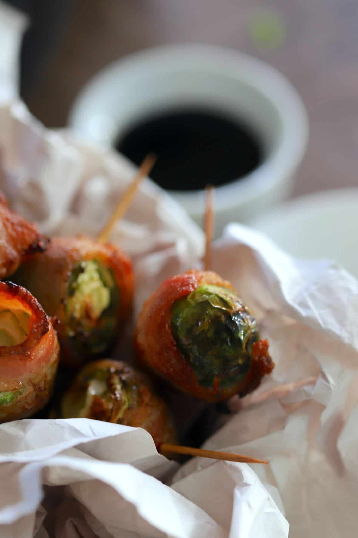 brussel sprouts wrapped in bacon with a toothpick inserted with a small bowl of soy sauce