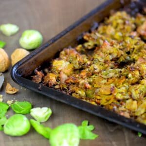 baked brussel sprouts on a baking sheet next to cracked walnuts with nutcracker and some brussel sprout leaves