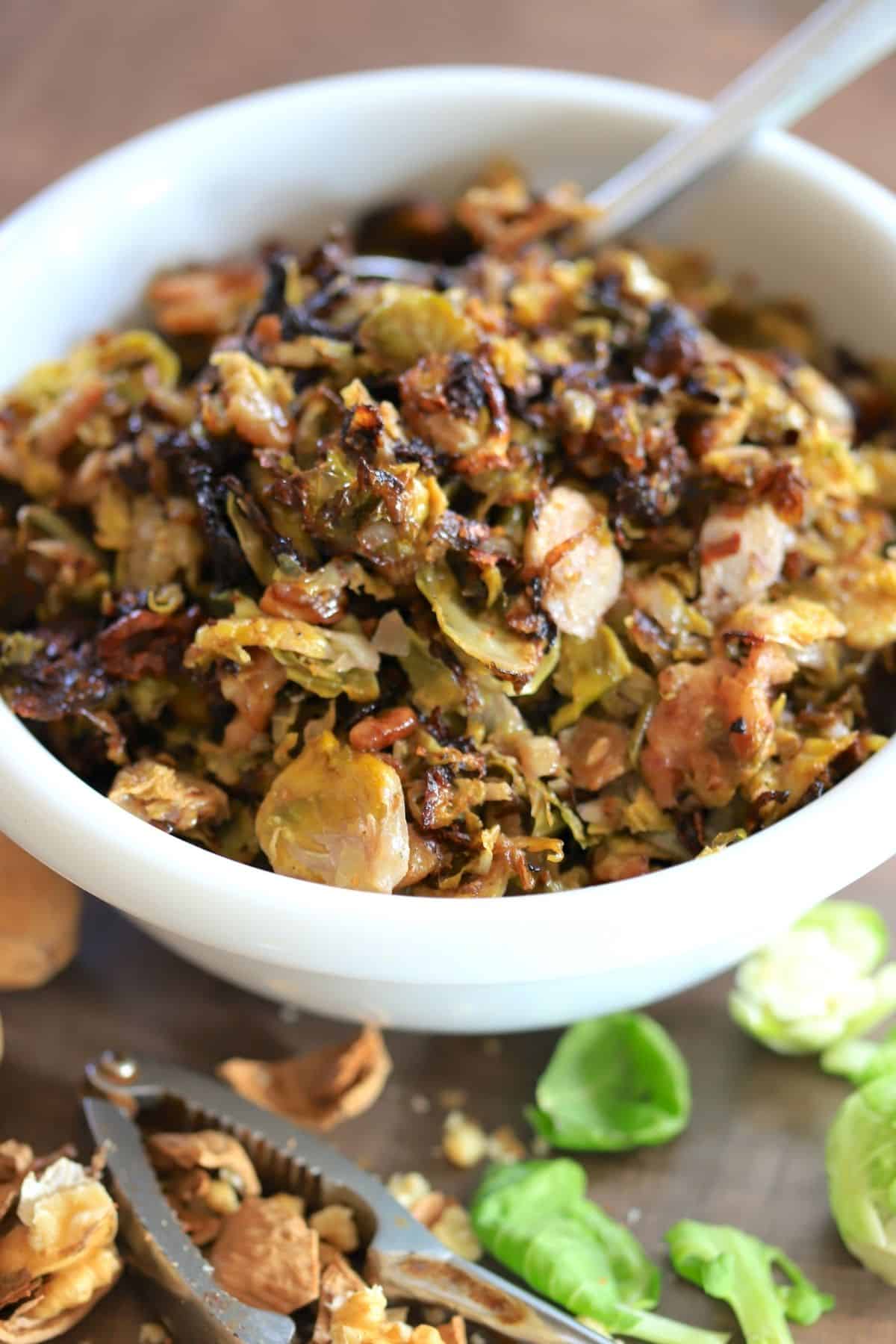 big white bowl with brussel sprouts next to crushed walnuts and brussel leaves