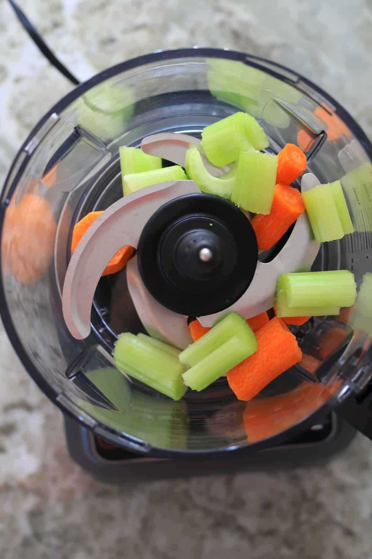 food processor with carrot and celery chunks in it