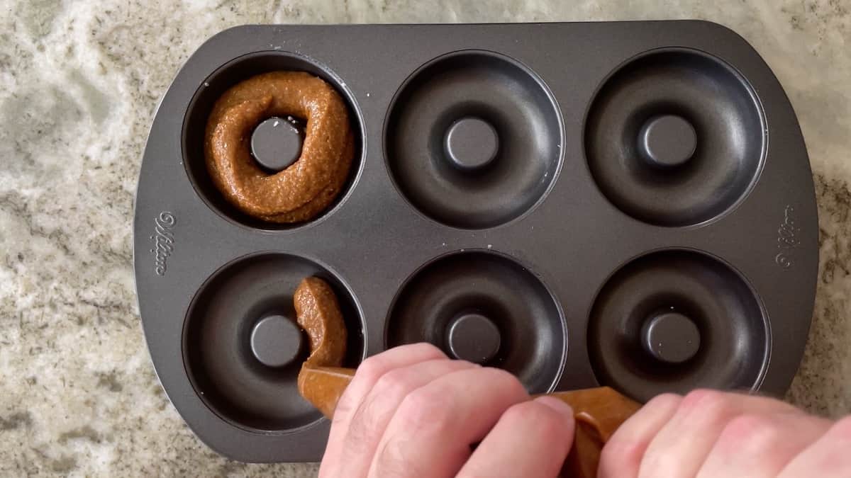 piping donut batter into donut mold pan