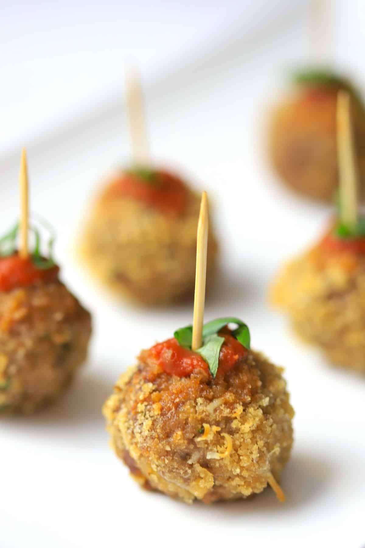 crispy meatballs on a white plate poked with a toothpick garnished with tomato sauce and basil