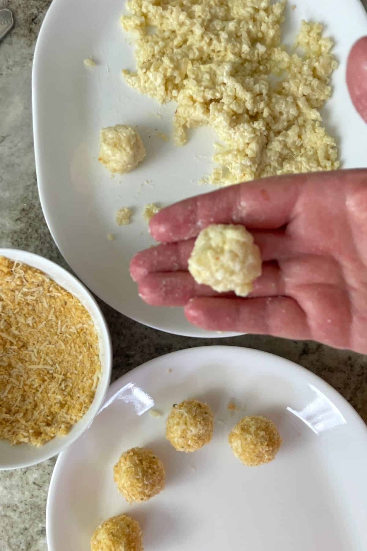 hand holding a fresh cauliflower ball over a plate of cauliflower rice, bread crumbs and breaded cauliflower balls