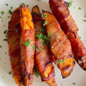 5 air fried low carb bacon wrapped sweet potatoes on a white plate with a parsley garnish