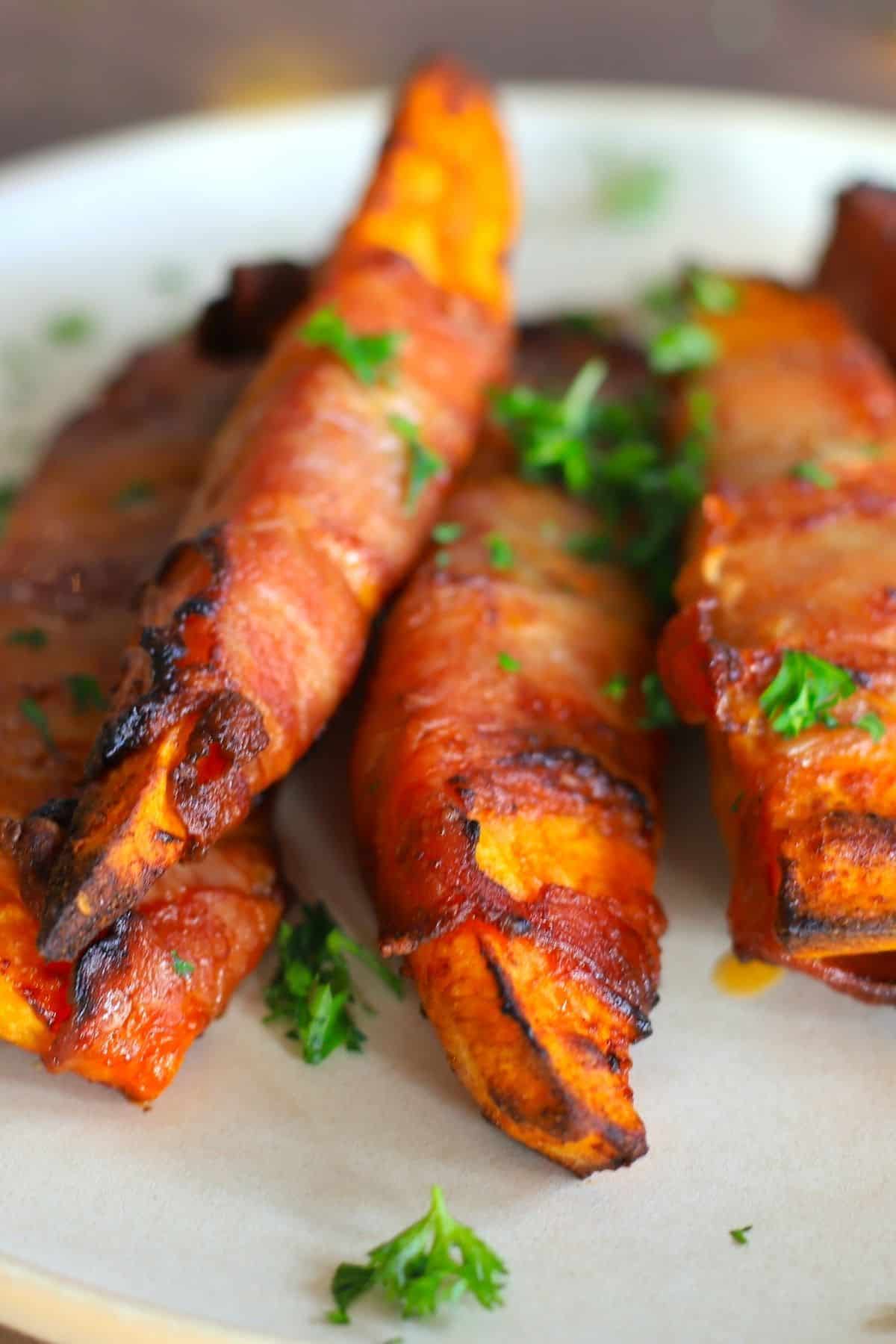 5 air fried low carb bacon wrapped sweet potatoes on a white plate with a parsley garnish