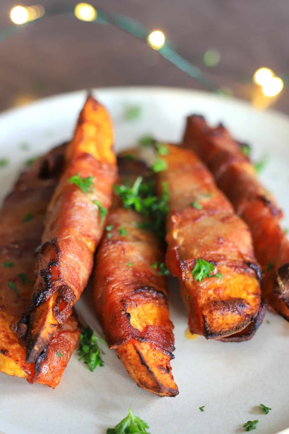 5 air fried low carb bacon wrapped sweet potatoes on a white plate with a parsley garnish