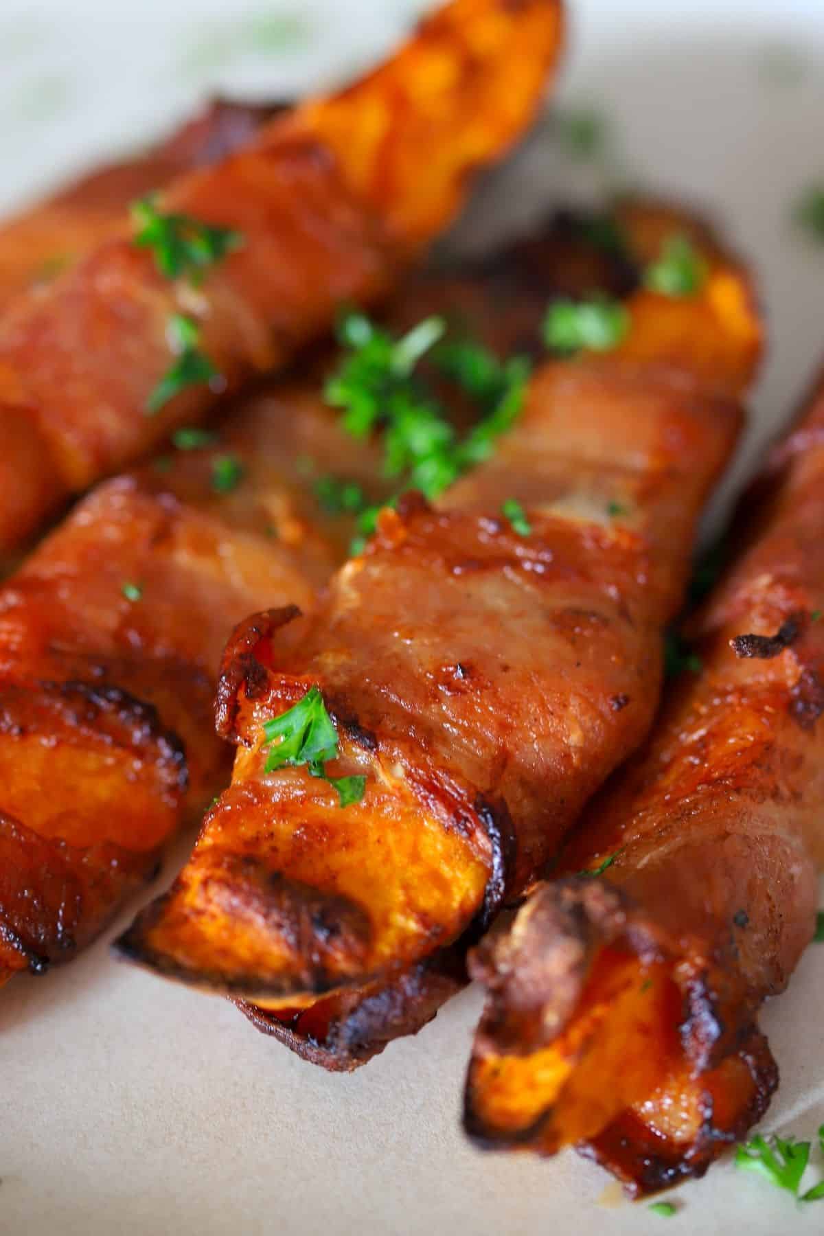 5 air fried low carb bacon wrapped sweet potatoes on a white plate with a parsley garnish