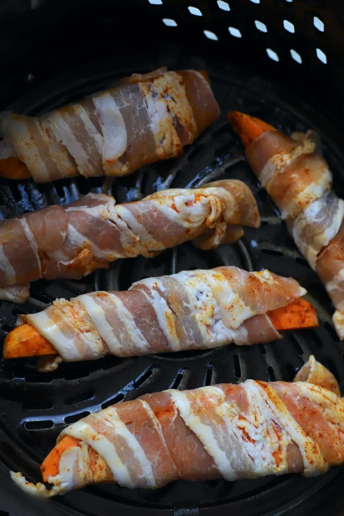 5 uncooked bacon wrapped sweet potatoe wedges in air fryer basket