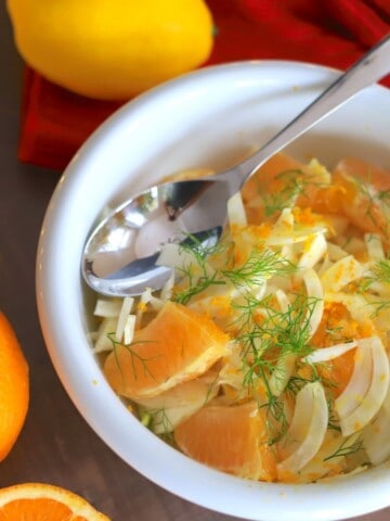 fennel salad in a white bowl with a spoon next to a lemon and orange