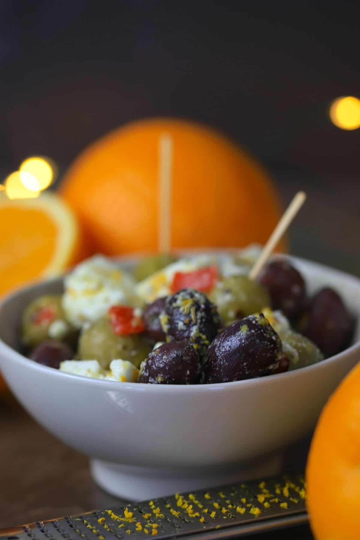 bowl of marinated olives and feta surrounded by oranges