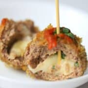 half a meatball with mozzarella in the centre topped with sauce basil and a toothpick