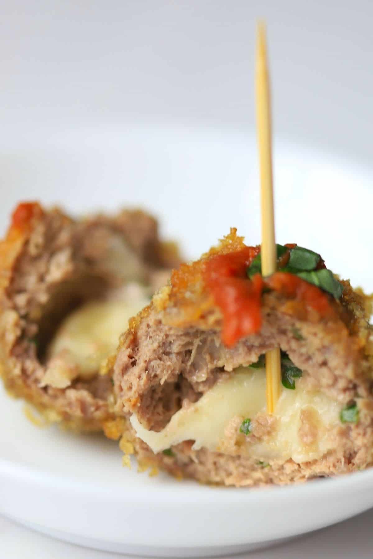 crispy meatballs on a white plate poked with a toothpick garnished with tomatoe sauce and basil