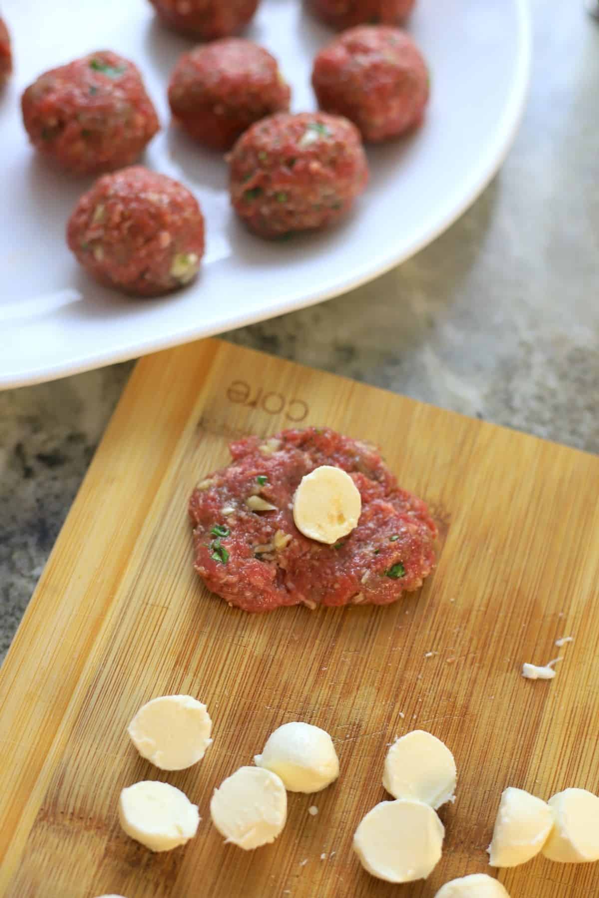 rolled meatballs on a white plate next to a flattened meatball with mozzarella in the centre next to slices of mozzarella balls