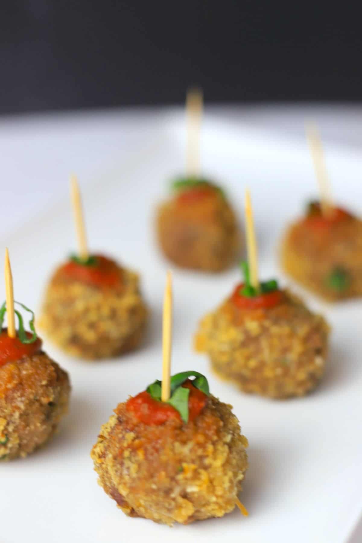 crispy meatballs on a white plate poked with a toothpick garnished with tomato sauce and basil