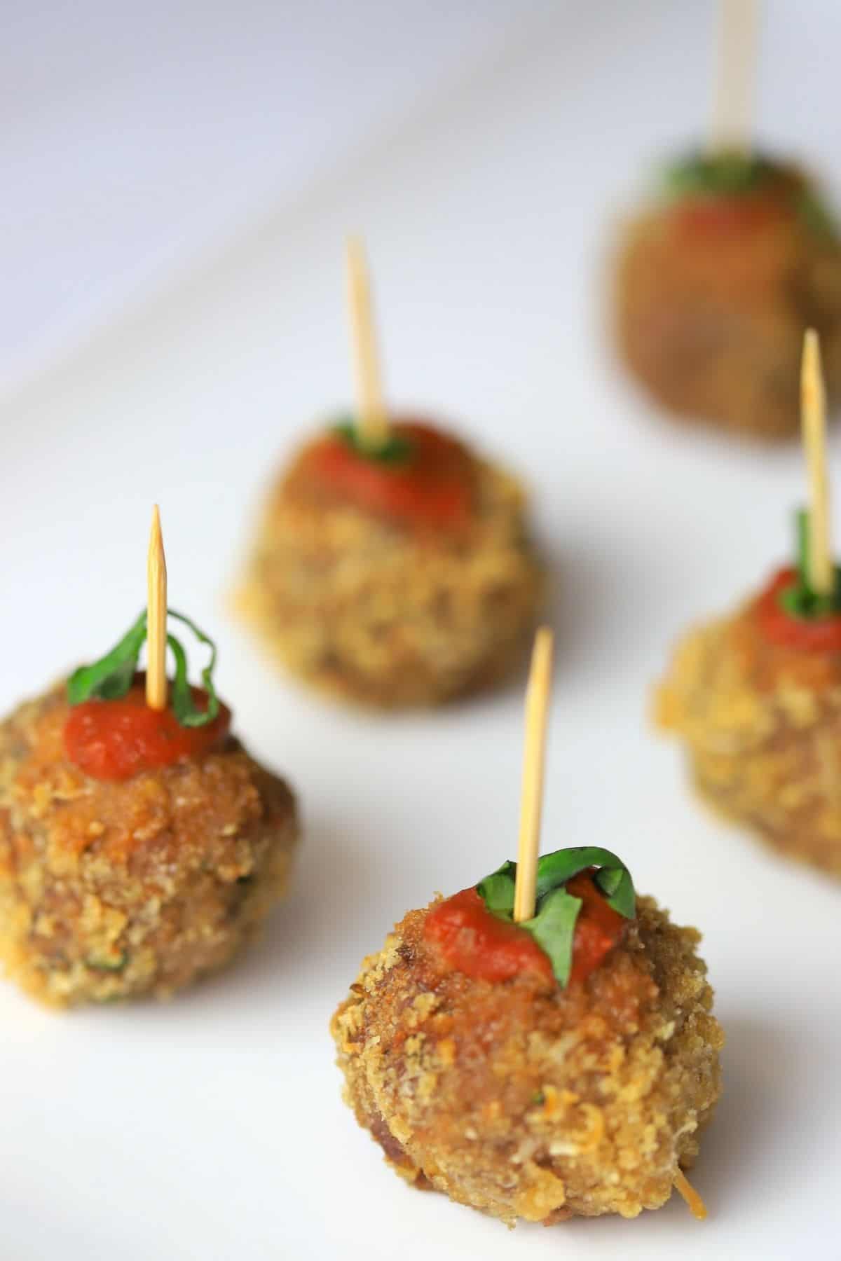 crispy meatballs on a white plate poked with a toothpick garnished with tomato sauce and basil