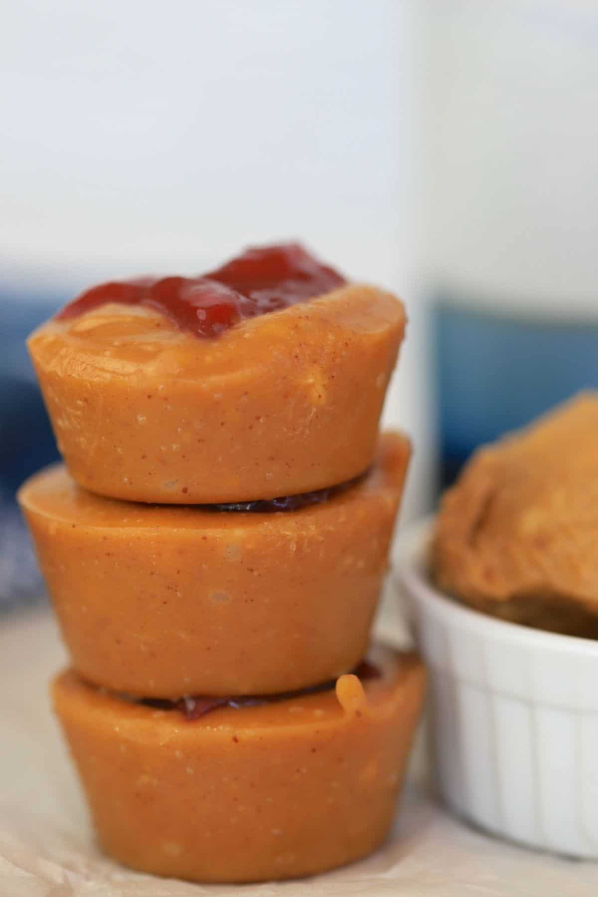 Sugar free peanut butter fudge bombs stacked on top of each other next to a bowl with peanut butter and a blue kitchen towel.