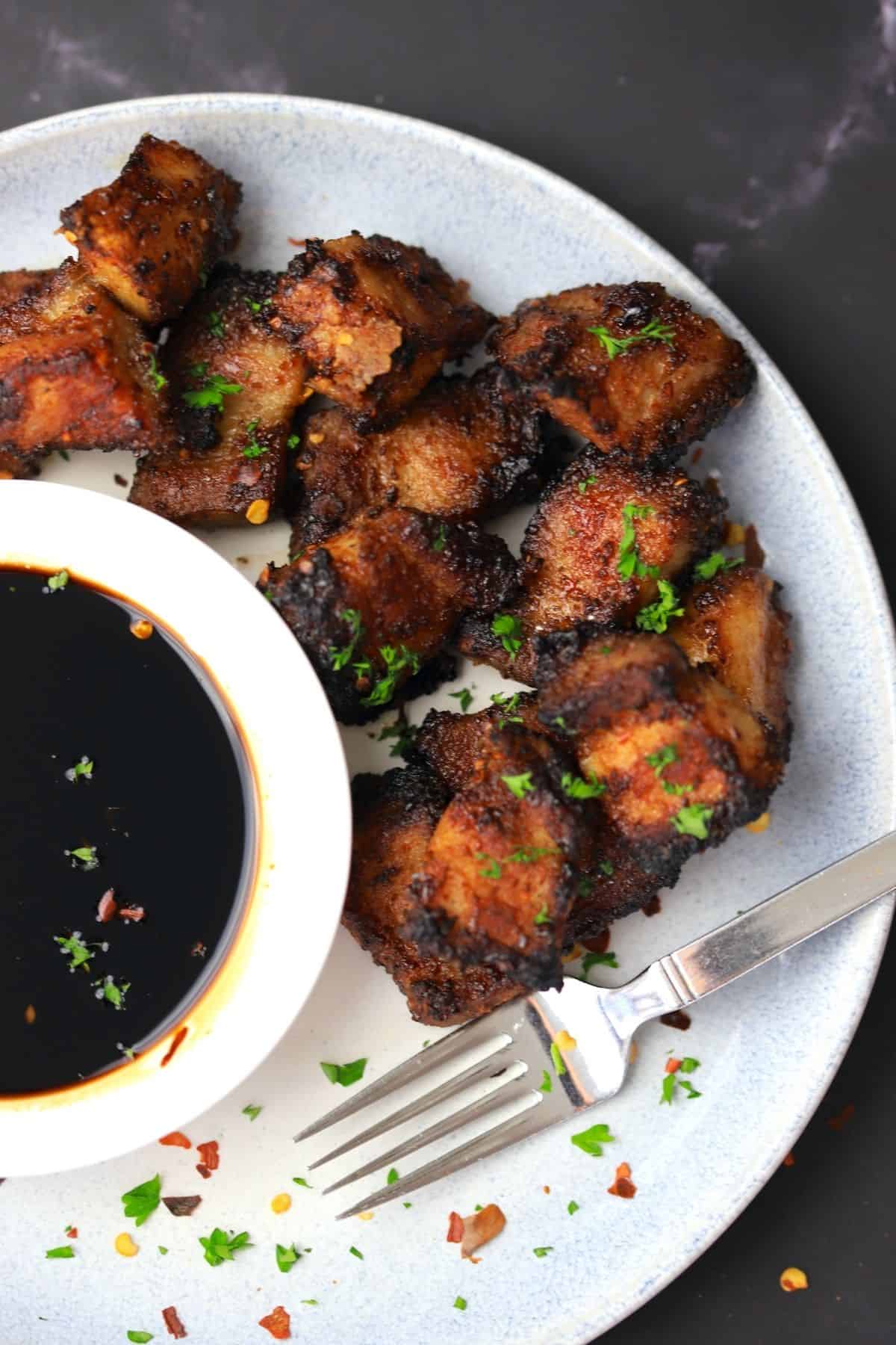 pork belly bites on a white plate sprinkled with parsley and chili flakes